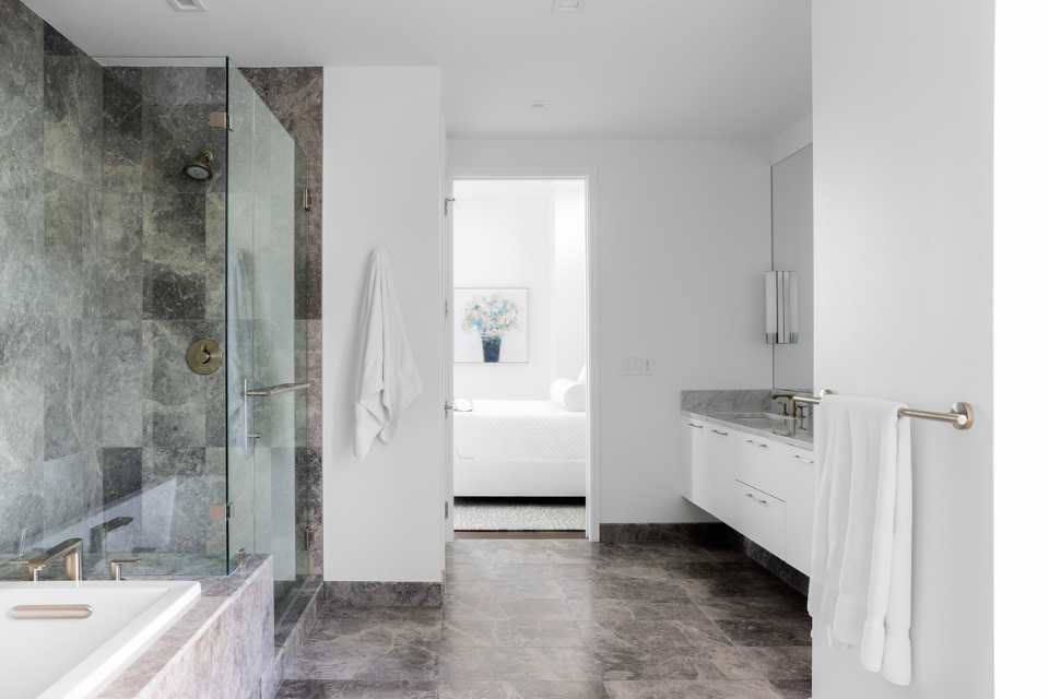 primary suite bathroom with natural stone floors and walls